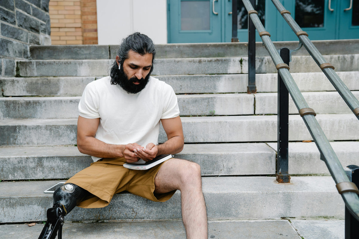 Man with a prosthetic leg sitting on steps using a smartphone